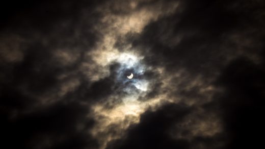 Wolken geben den Blick auf einen leuchtenden, sichelförmigen Mond.